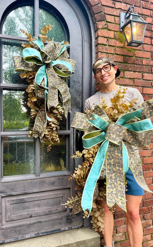 Handmade JME fall door swag made with faux brown eucalyptus. Paired with a beautiful floral grey and teal JME bow. About 3 feet long by 21 inches wide. *Some fluffing may be required upon receiving.