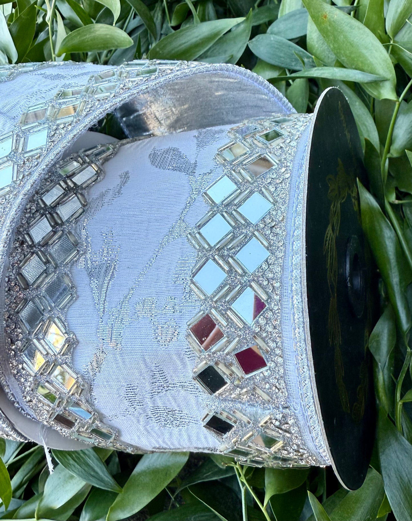 JME Heavy wired ribbon. White/silver leaf vine ribbon with mirrored diamond trim work. Back with silver metallic. 4“ x 5 yards.