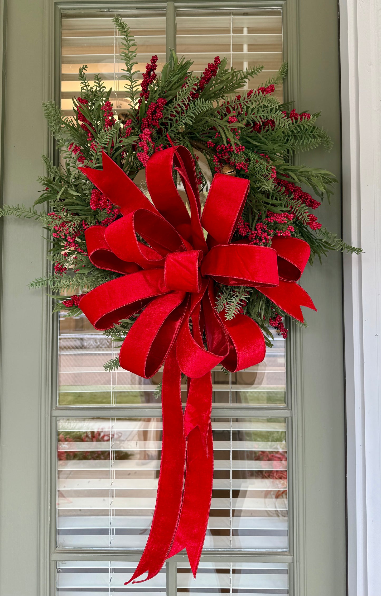 Jingle bell and faux berry wreath. Tied with a JME red velvet bow. About 24 inches wide.