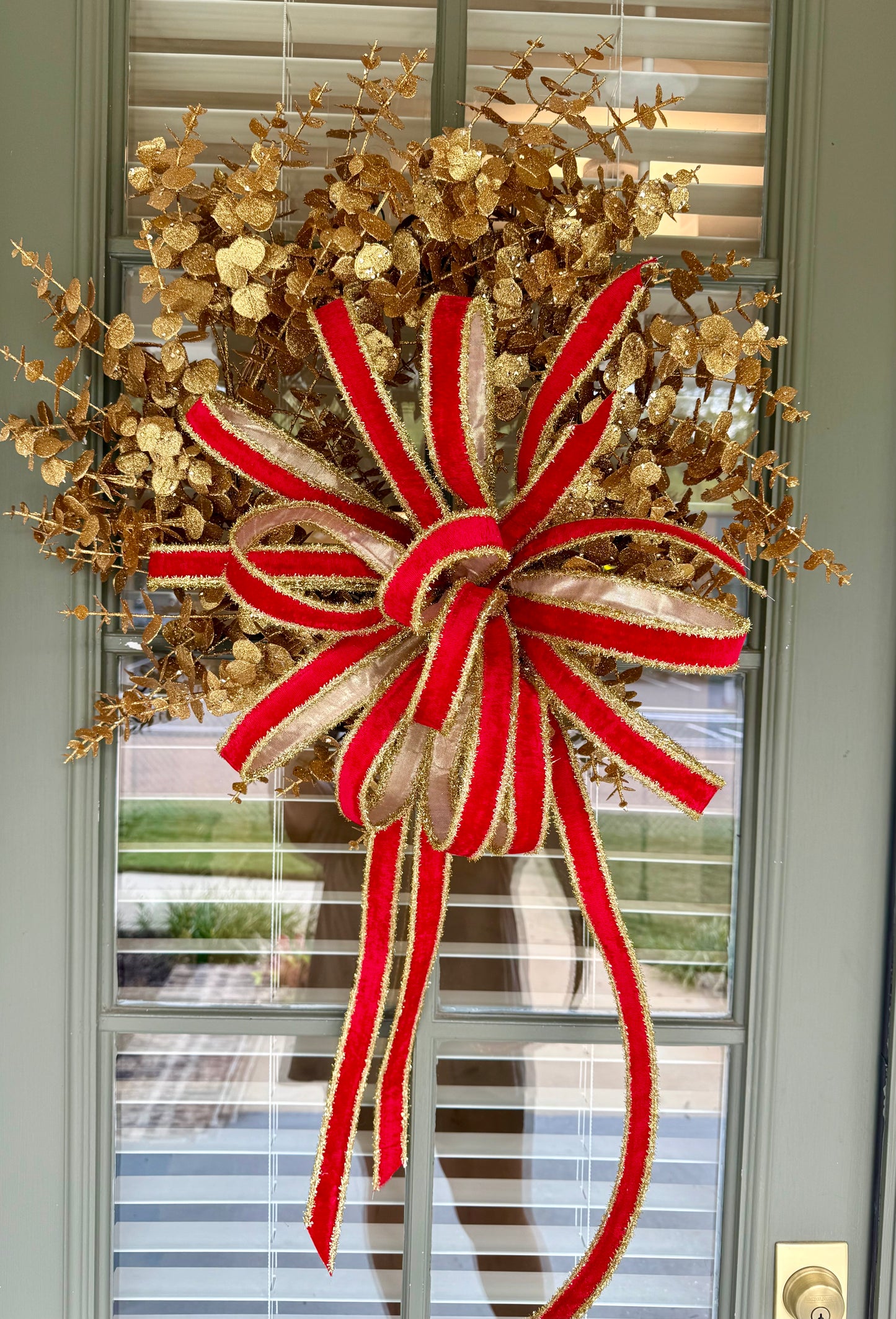 Glittered gold faux eucalyptus. Tied with a JME red velvet and gold tinsel bow. About 20 inches wide.