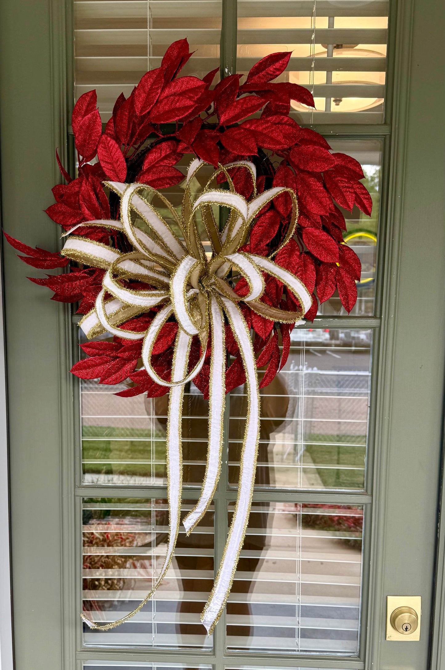 Glittered red faux leaf wreath. Paired with a JME white velvet and gold tinsel bow. About 20 inches wide.