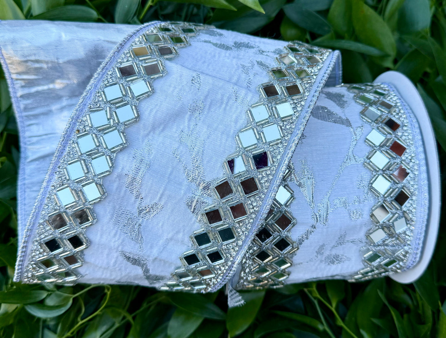 JME Heavy wired ribbon. White/silver leaf vine ribbon with mirrored diamond trim work. Back with silver metallic. 4“ x 5 yards.