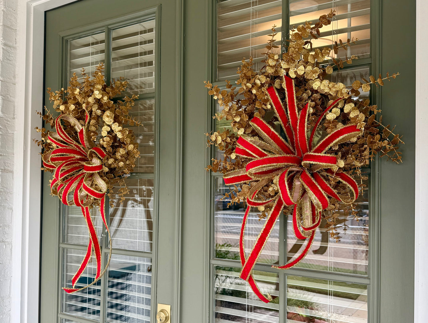 Glittered gold faux eucalyptus. Tied with a JME red velvet and gold tinsel bow. About 20 inches wide.