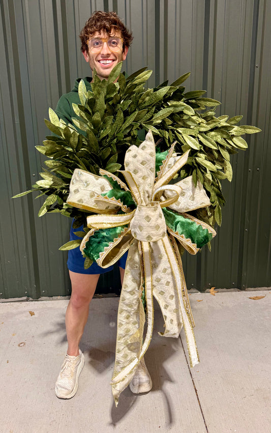 Green and gold faux bay leaf wreath. 30 inches wide. Paired with a JME handtied blue velvet tied bow of white and green velvets.