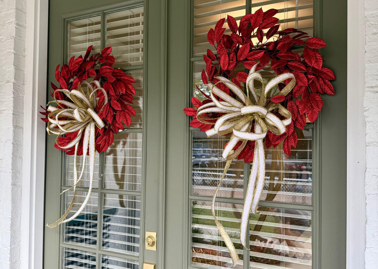 Glittered red faux leaf wreath. Paired with a JME white velvet and gold tinsel bow. About 20 inches wide.