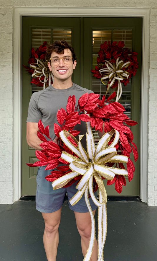 Glittered red faux leaf wreath. Paired with a JME white velvet and gold tinsel bow. About 20 inches wide.