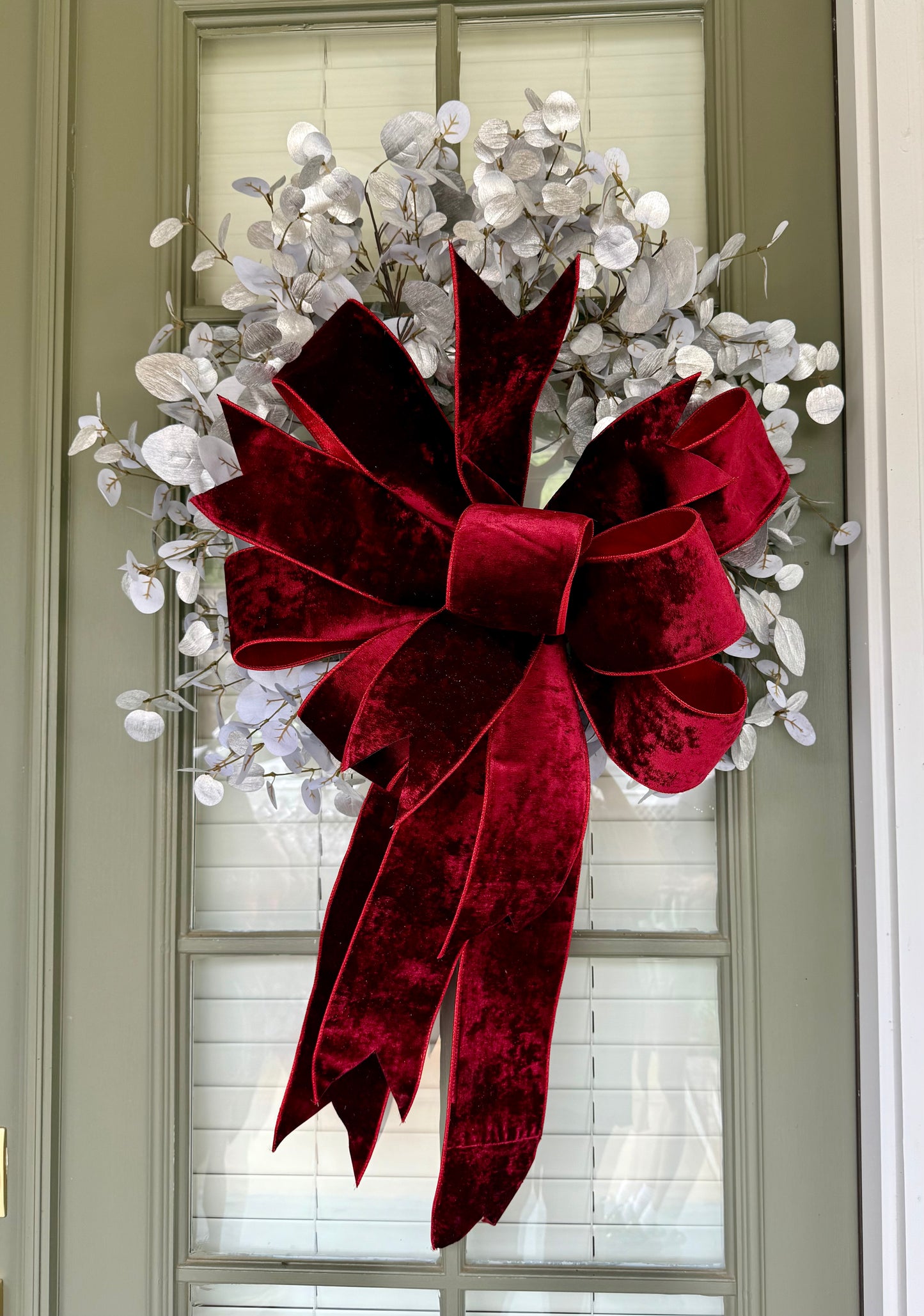 Faux silver eucalyptus wreath with hand tied JME deep red velvet bow. About 24 inches wide.