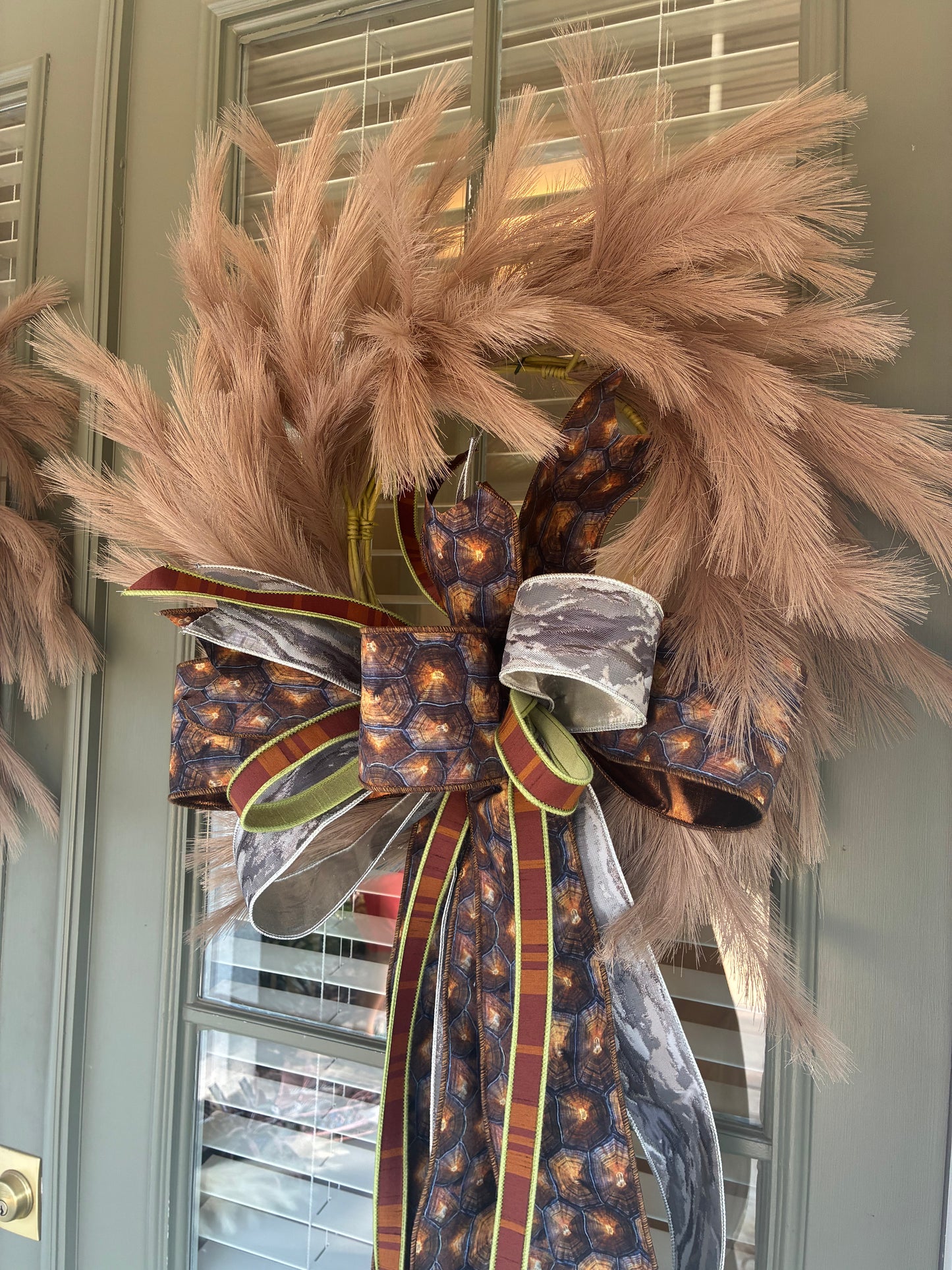 Faux Taupe Plume Wreath paired with a JME hand tied bow featuring a brown and silver fall colored ribbon combo. Approximately 26 inches in diameter. Some fluffing may be required upon arrival.